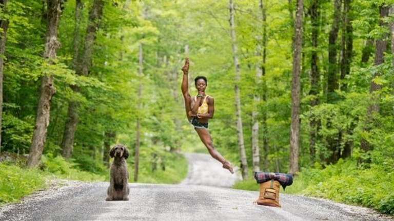 A woman doing acrobatics on a road with a dog and backpack on either side