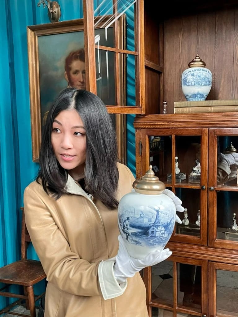 A woman holding a porcelain vase while wearing gloves and a tan coat