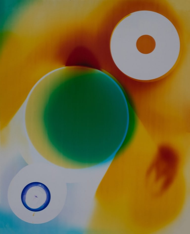 Three circular shapes lined up diagonally from left to right, bottom to top. The top right one has an orange circle in the center, the middle one a green and yellow hue and the bottom left one has a blue ring within. There are green, orange, yellow red and blue tones dispersed throughout the image. 