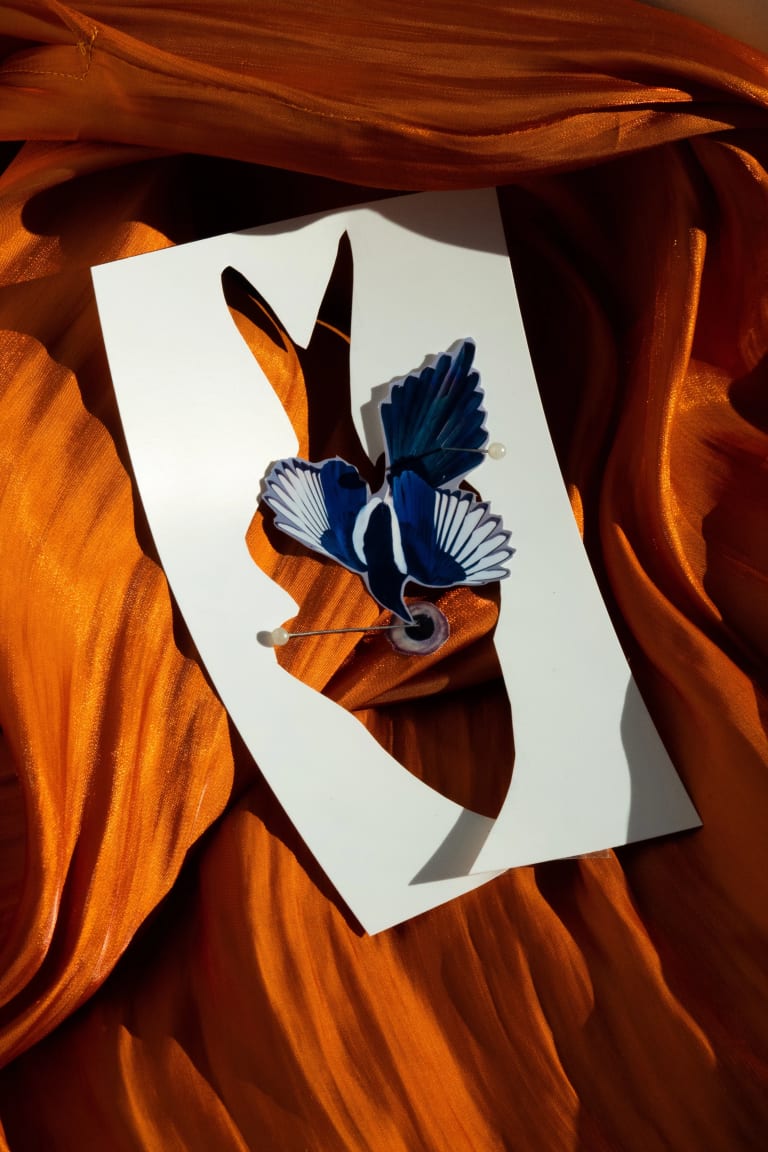 An abstract photograph collage of a blue bird, a cut out of paper resembling a fish on an orange backdrop.