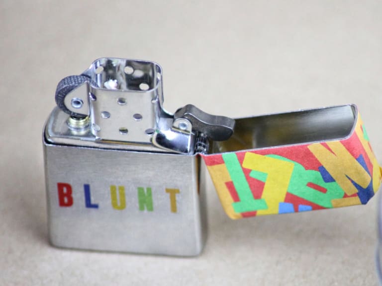 A vintage chrome zippo liter with the words "BLUNT" written on them in color with a colorful top. 