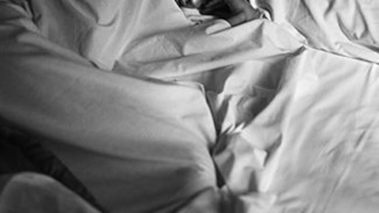 Black and white photo of a woman under white sheets in bed.