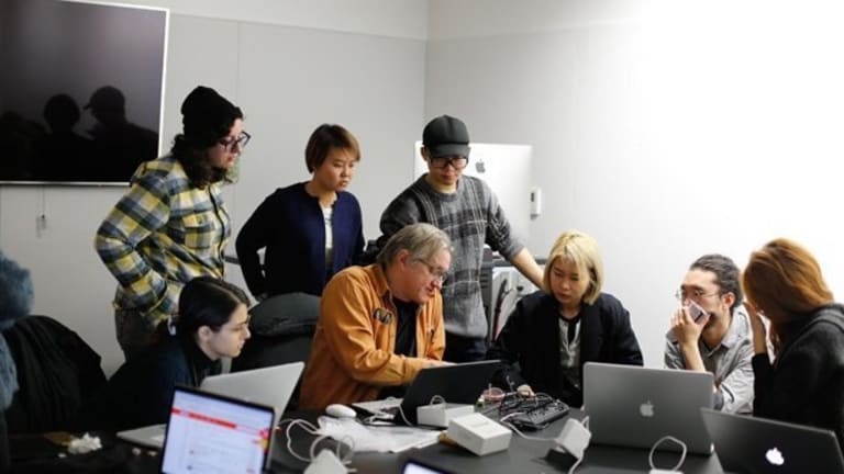 Men and women in a meeting. Everyone is at one end of the table and looking at a single laptop screen.