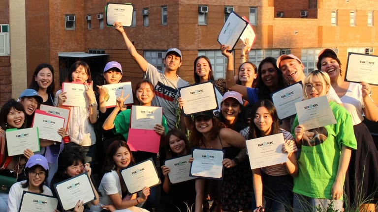 Several students holding up diplomas outside a New York City building