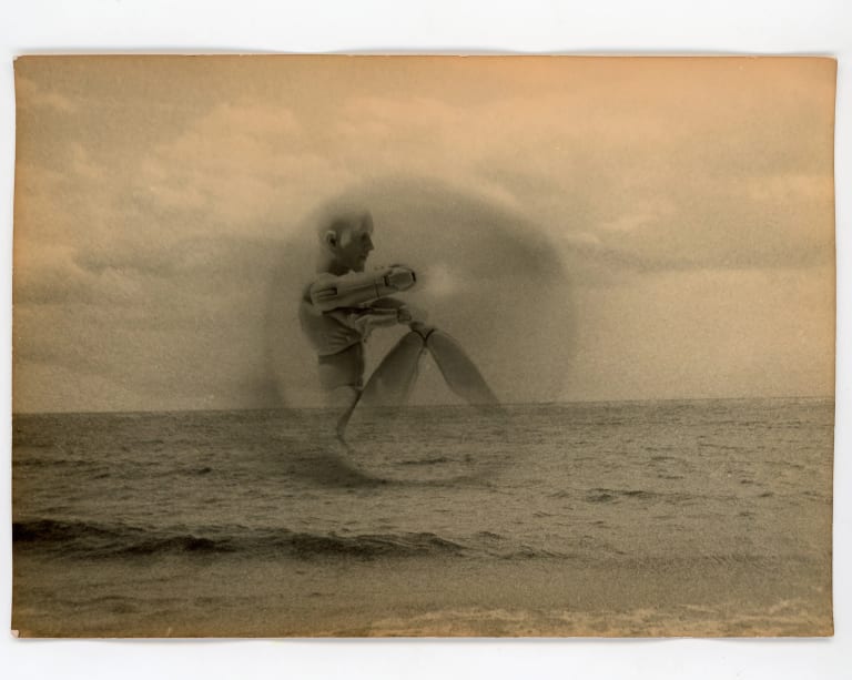 Photograph depicting wooden figure toy in a bubble floating over the ocean.