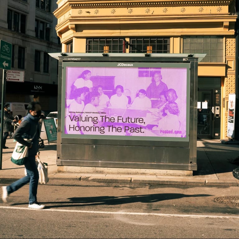 a purple billboard on a green newsstand says, "Valuing the Future, Honoring the Past" alongside an image presumably from an NAACP meeting in the 1960s.