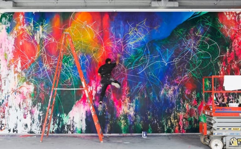 A man paints on a brightly colored graffiti wall.