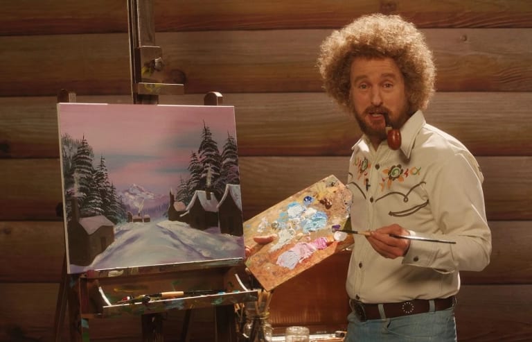 A film still of a man with blonde curly hair, smoking a pipe, standing in front of a painting with a painter's palette.