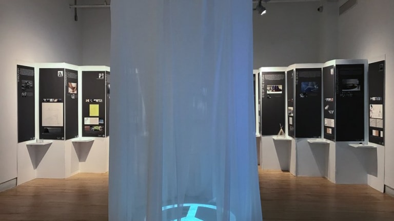 a thin see-through curtain descending from the ceiling in a circular shape. In the middle of the shape is an illuminated peace sign on the floor.