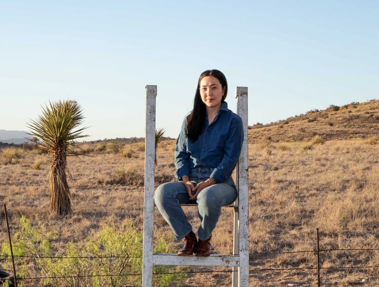 Image of Daisy Nam sitting on a fence in the desert