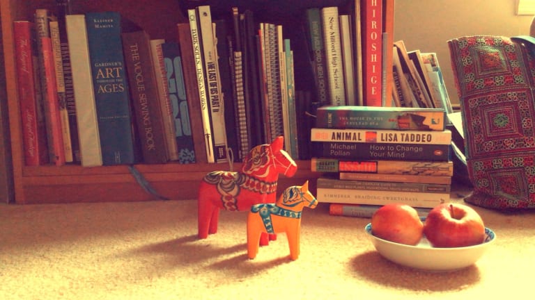 Here is a film still of two horse figurines standing in front of a row of books.