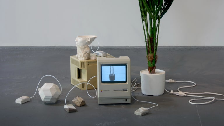 Sculpture with 1990s computer, 3D print white heads and houseplant on a grey floor with a white background.