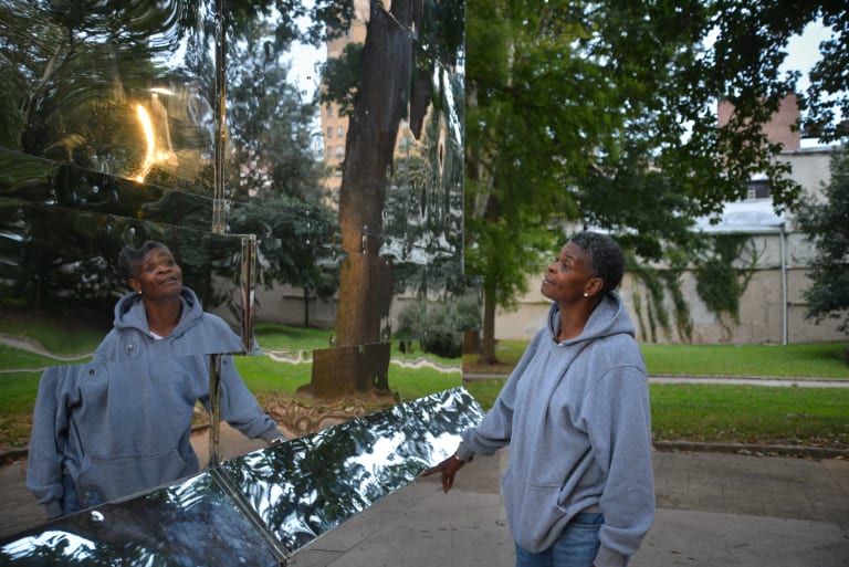 Image of a woman in a grey sweatshirt looking at her reflection in a mirrored sculpture in the park. The Battle Is Joined, Monument Lab, Mural Arts, Public art commission, Vernon Park, Philadelphia, PA, 2017