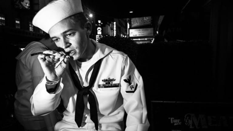 A man in the Navy smokes a cigarette while gazing downward