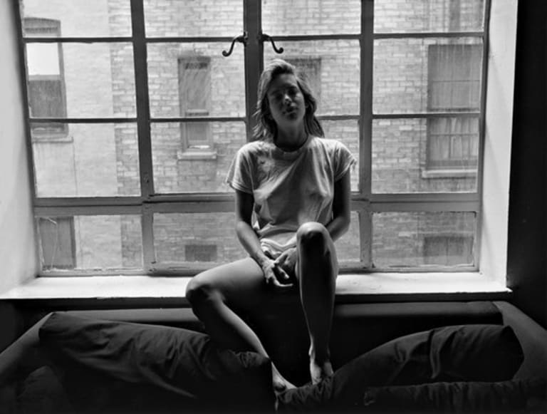 A woman sits on the window sill with her legs on the sofa.