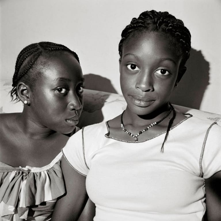 Two young african american women with cornrows seated on a couch.