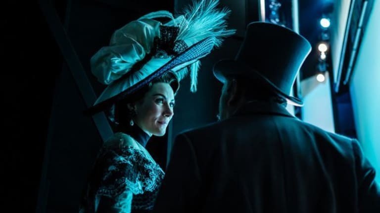 A woman in 19th-century clothing and an elaborate hat looks at a man who is facing away from the viewer and wearing a top hat.