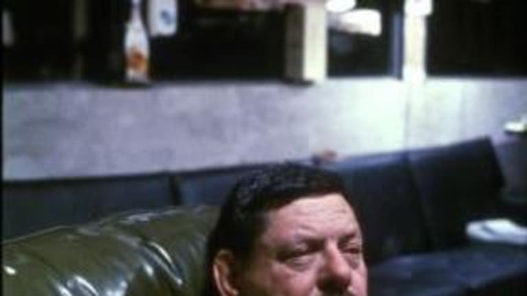 A man sitting on a green couch, gazing into the distance.  The background is slightly out of focus.
