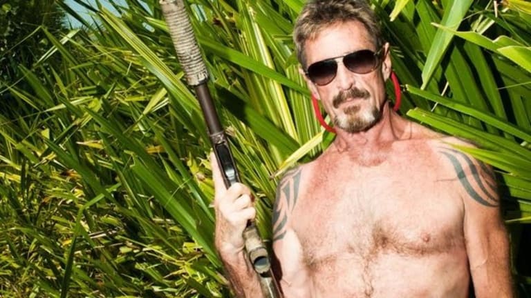 A shirtless tatooed man with sunglasses holding a rifle in a jungle.