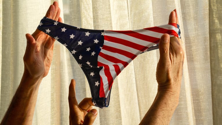 Three human hands extend to hold and stretch taut spandex underwear printed with a pattern based on the American flag.