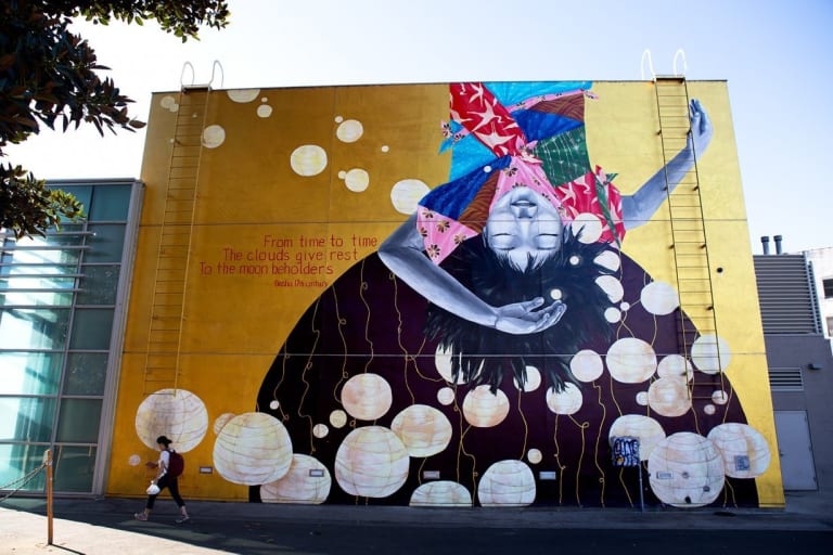 A colorful mural of a person hanging upside-down with their eyes closed, surrounded by floating lanterns