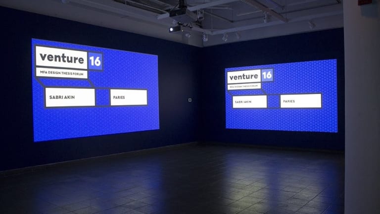 In an empty tiled floor room there are two large presentation monitors, both depicting the same image. It presents a blue slanted grid  screen of "Venture 16" for the MFA Design Thesis Forum by Sabri Akin.