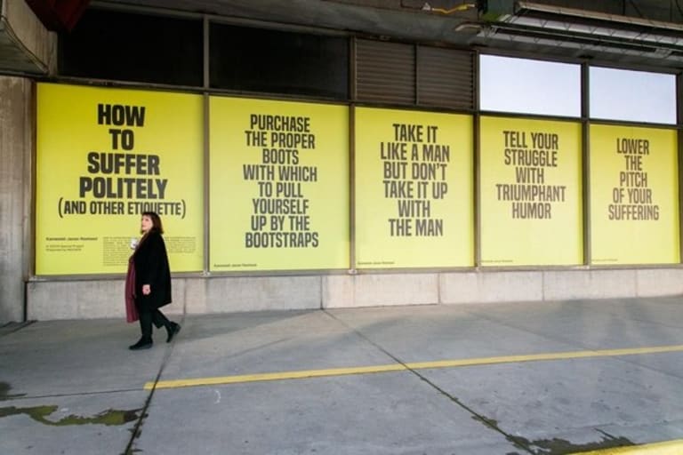 A woman walks down the sidewalk alongside yellow and black posters containing sayings of advice.