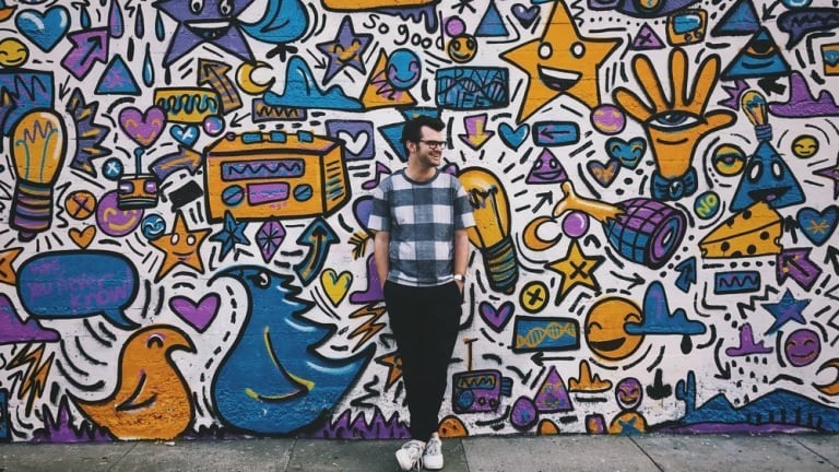 A full body shot of a man standing on a sidewalk against a vibrant mural