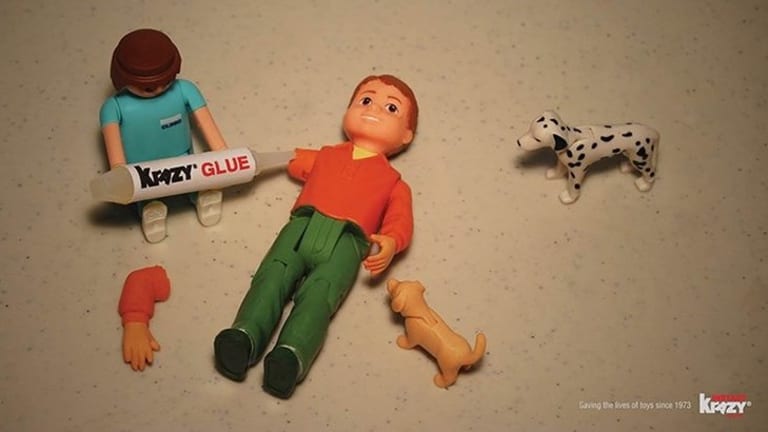 Two action figures and two dogs on the floor. There is a stick that says "Krazy Glue".