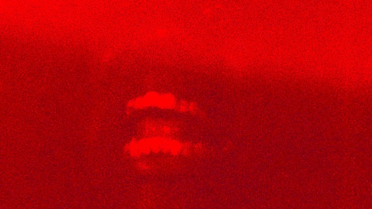 A red image of a person's face, the upper half of the face is obscured and you can see an open, smiling mouth