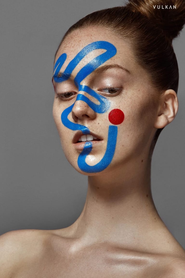 A photograph of a woman with yellow and blue paint on her face shot by Ruo Bing Li for Vulkan Magazine.