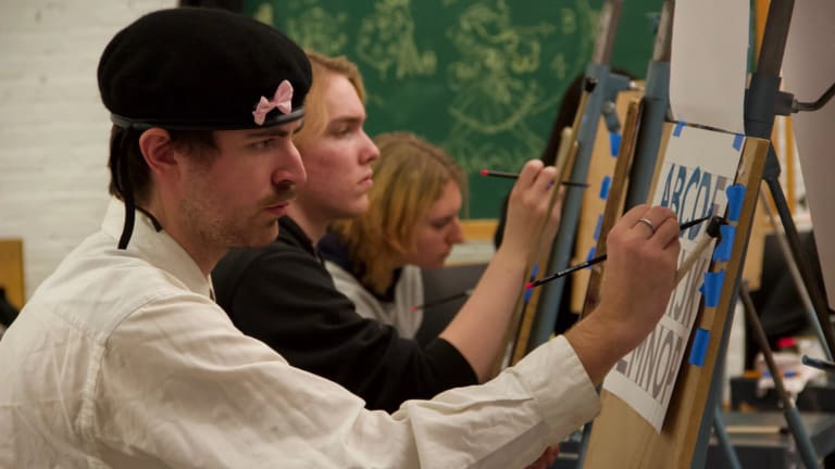 Three students tracing letters with paint as part of the Hand Lettering and Sign Painting spring workshop.