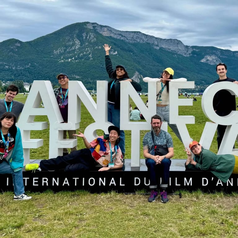 People, smiling, and raising their arms, pose in front of the Annecy Festival sign in France. 