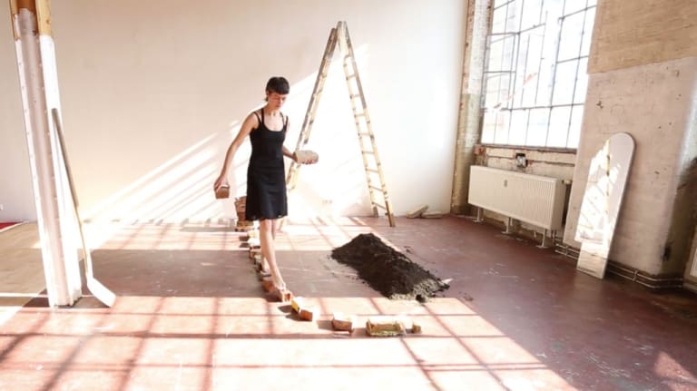 A woman in a dress stepping on individually placed bricks in an art studio