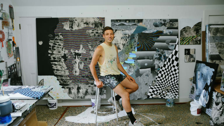 Photo of Will Hutnick sitting on a stool in studio with artworks