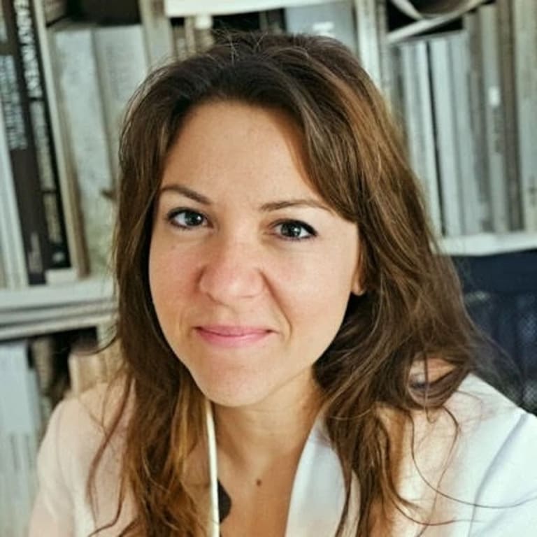 Photo of iLiana Fokianaki, a woman with long brown hair and brown eyes who is looking directly at the camera 