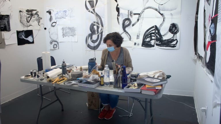 artist in resident working in studio with black and white ink drawings pasted on walls