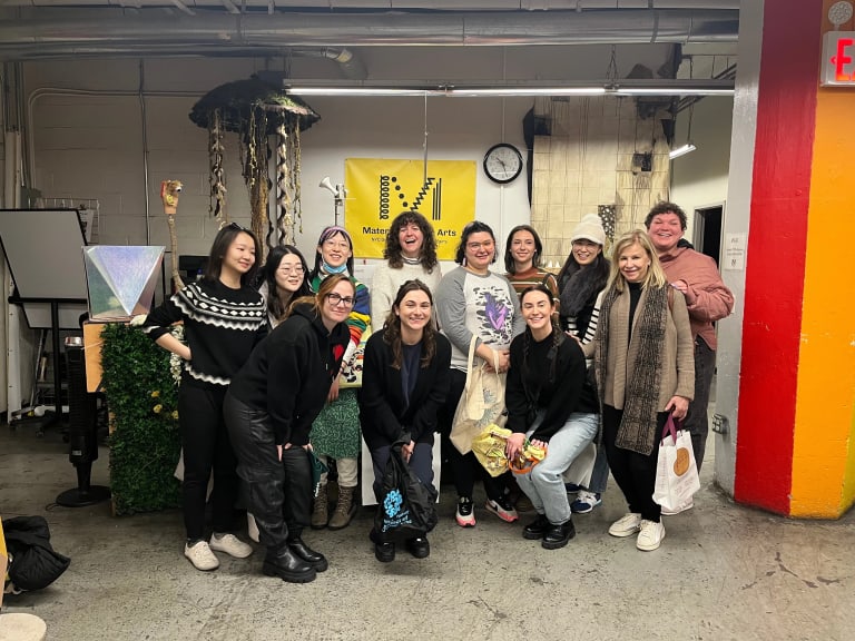 A group of smiling MPS Art therapy students gather in front of a Materials for the Arts sign. 