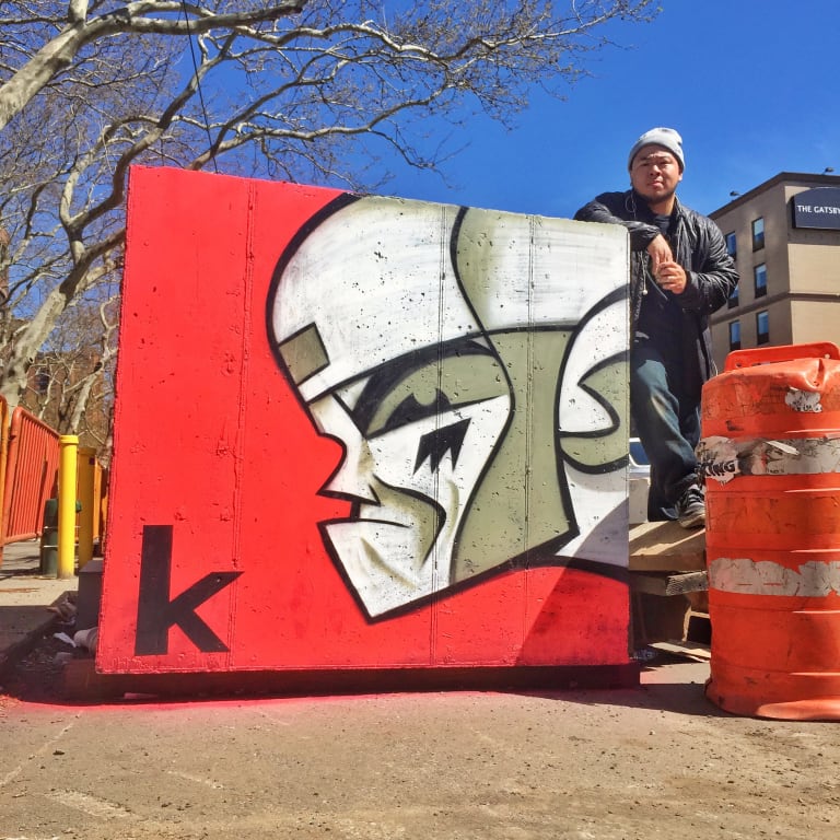 A photograph of KaNO Kid posing next to one of his art pieces