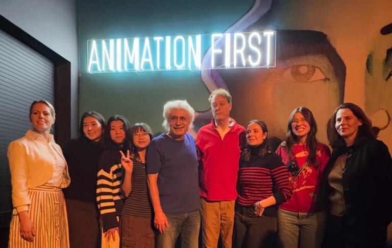 Nine people standing in front of a neon sign that says "Animation First"