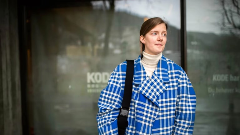 Ingrid Haug Erstad in front of a glass storefront wearing a blue plaid coat and looking away from the camera