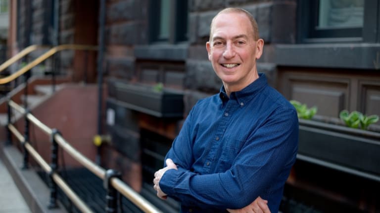 In a blue, collared shirt and with arms folded, Jim Arnoff smiles for the camera while standing on the sidewalk of a NYC street.