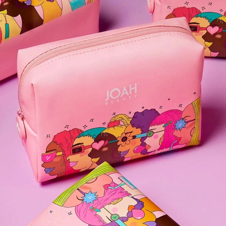 A pink beauty bag with a diverse and animated array of women illustrated on it with sunglasses and colorful hair on a pink background.