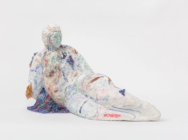 A sculpture of a reclining figure made of plaster, fabric, and pigment. The figure is white with stains of many different colors across its surface.