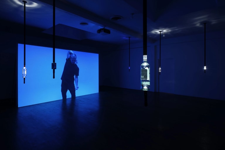 Image of projected video with man dancing and bottles of vodka hanging from the ceiling.