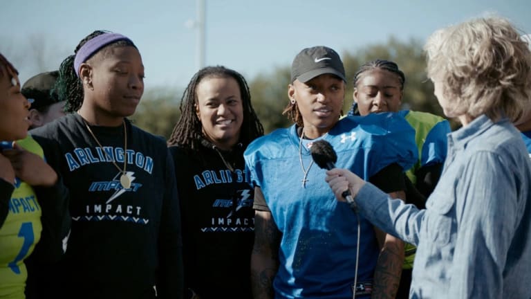 A video still featuring several teammates on a women's football team speaking with a woman who is holding a microphone out to them.