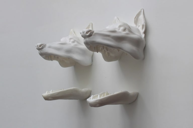 Sculptural installation featuring two open-mouthed dog heads attached to the wall.