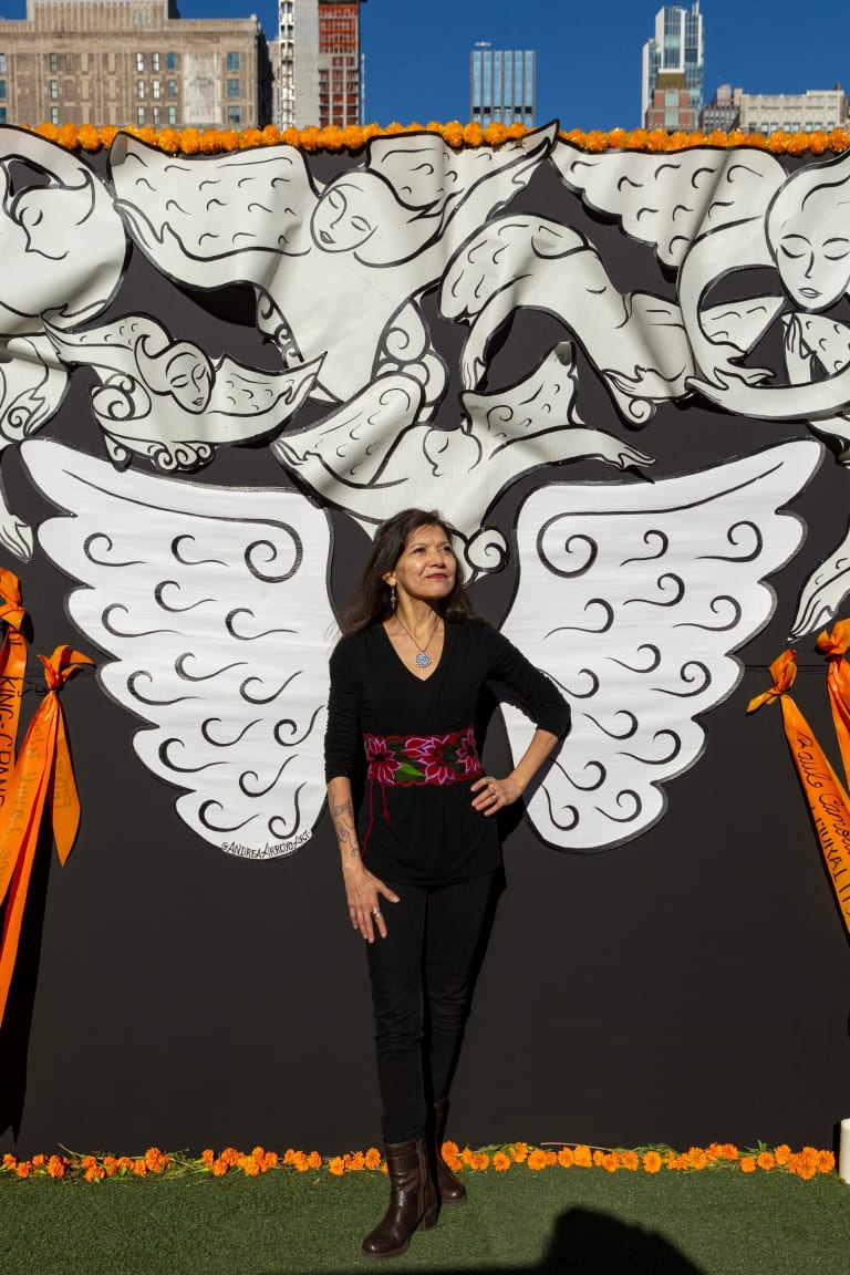 Artist Andrea Arroyo standing with the wings at the back of the community altar. 