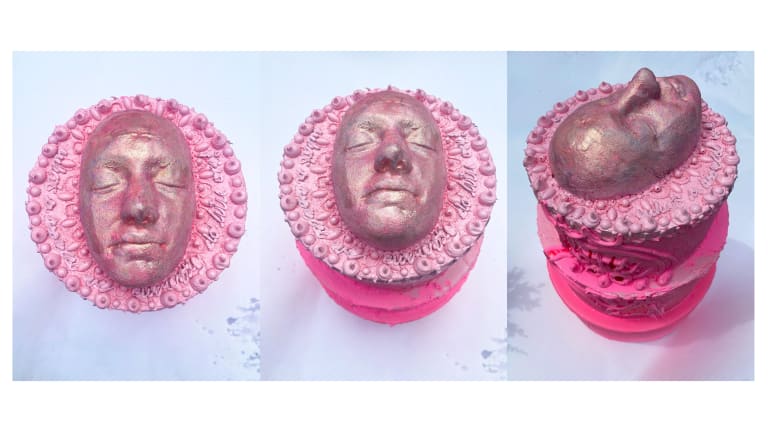 Pink sculpture of a face with decorative elements around the face. 