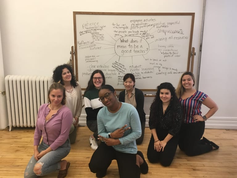 A group of people kneels and poses in front of a white board covered with writing